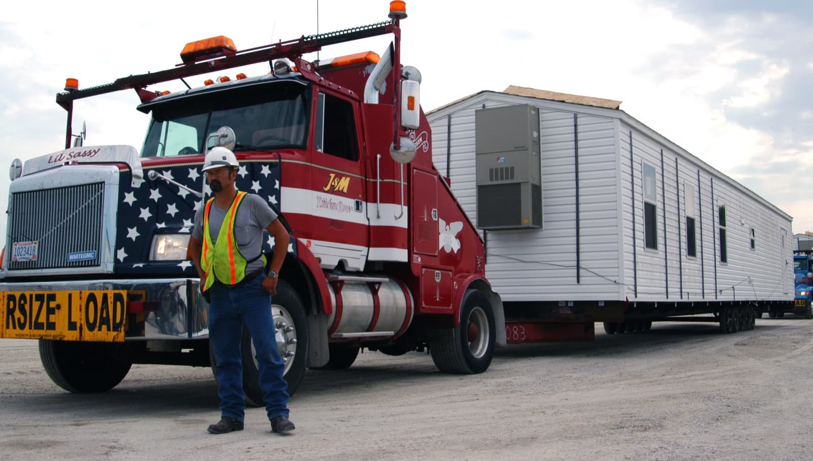 A toter truck with an oversize load banner hauling a manufactured home section along a highway