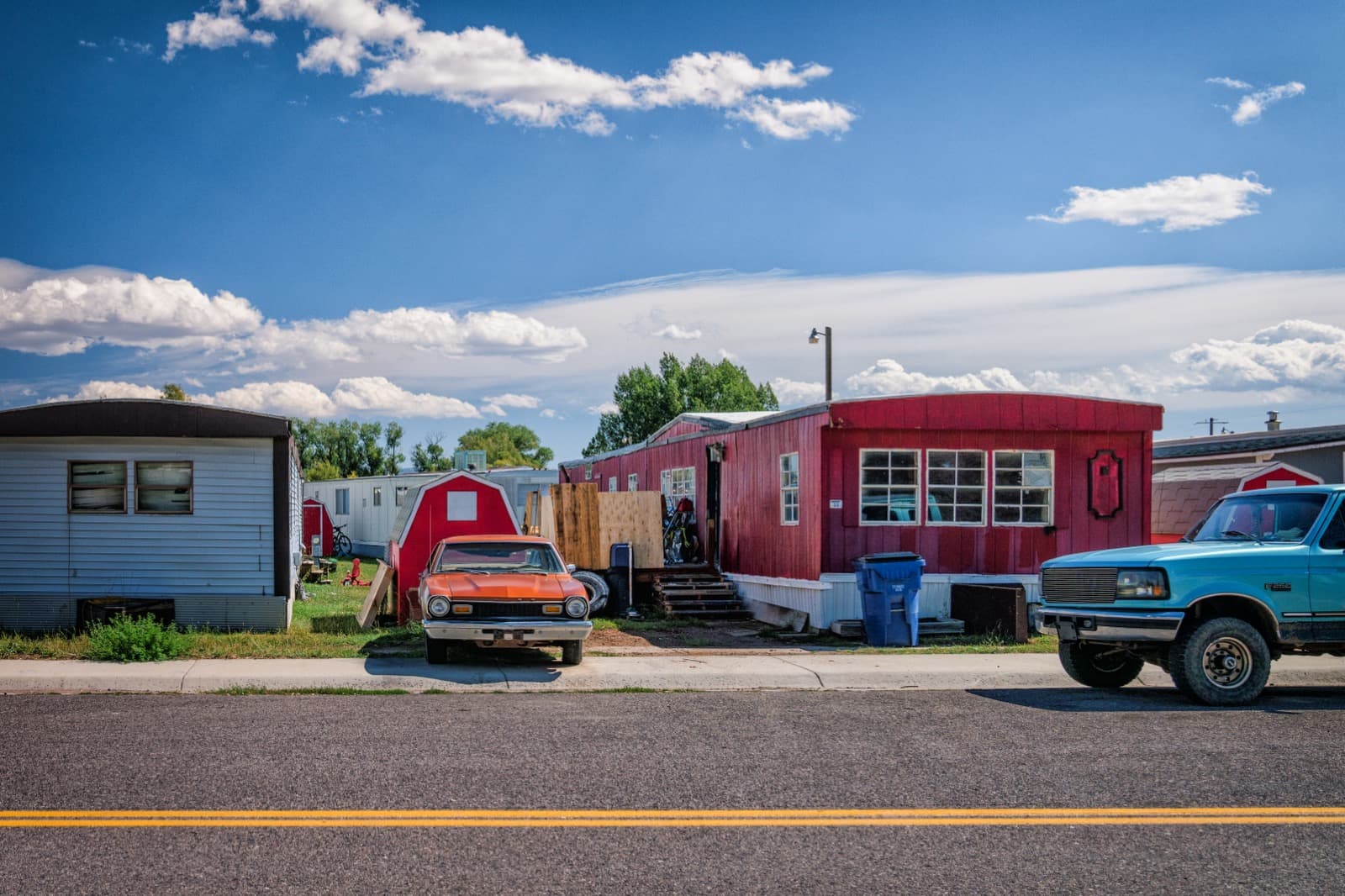 A single-wide manufactured home with a pickup truck parked outside under a blue sky